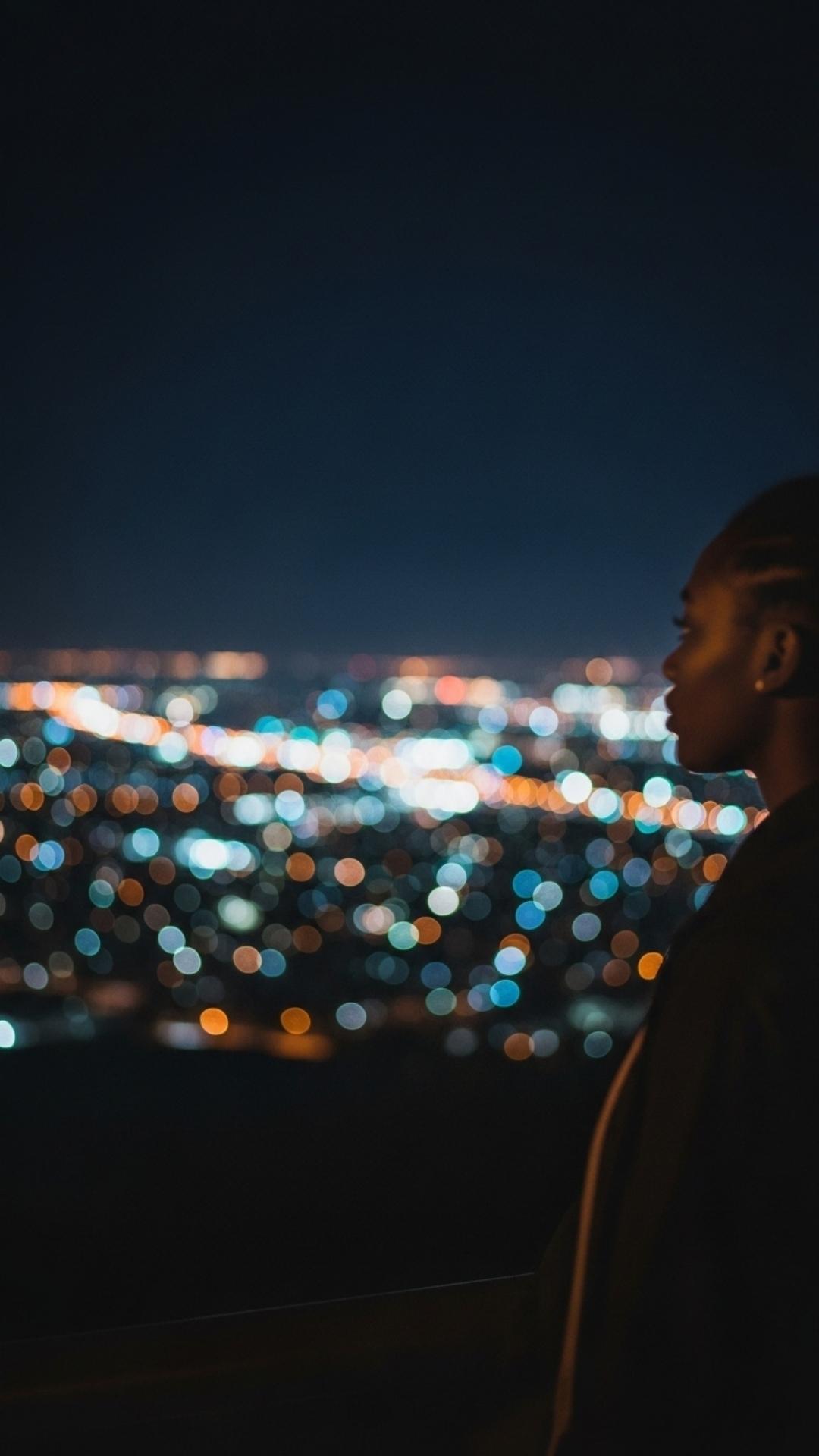 Blurred city lights at night with a distant, out-of-focus figure, conveying urban loneliness and a pensive mood.