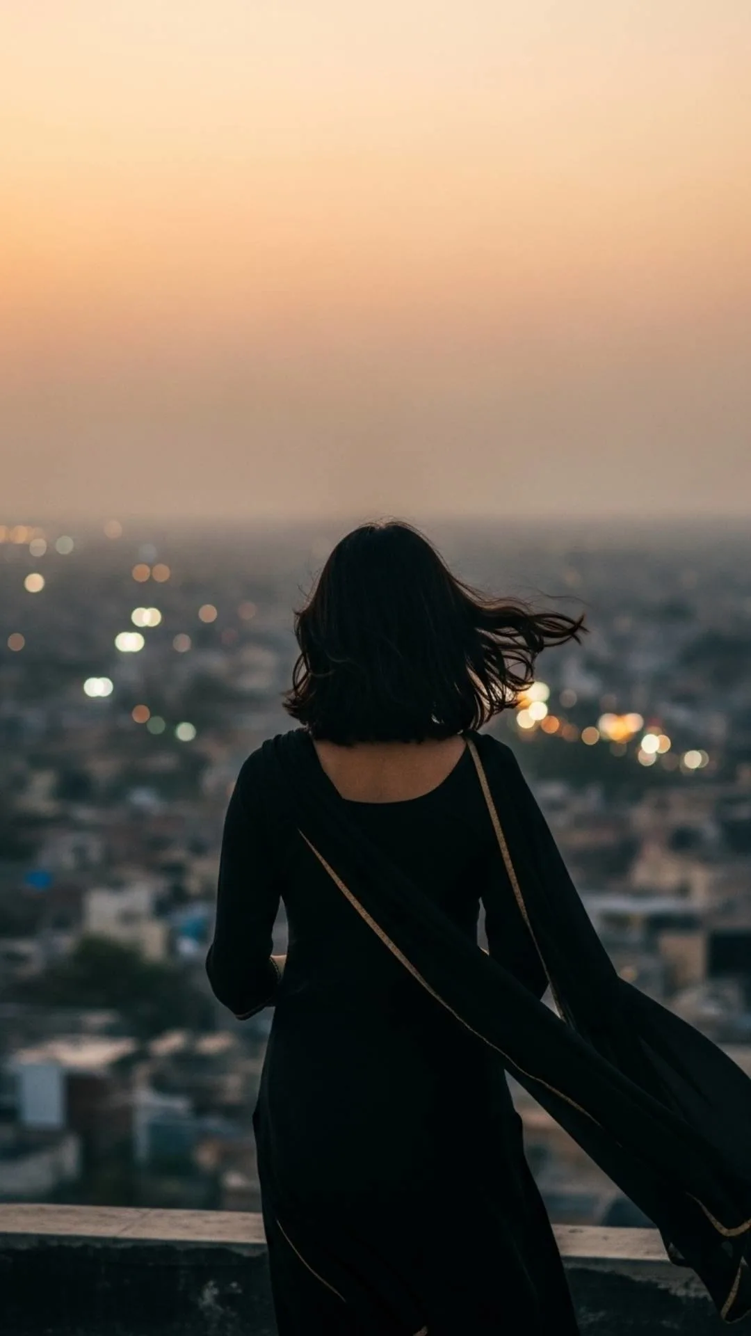 Silhouette of a lonely girl looking at city lights from a rooftop, a mood off profile picture for Instagram.